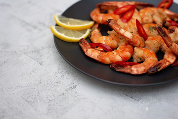 Tasty cooked fried shrimp with chilli and lemon on a gray concrete background. Healthy seafood. Copy space. Flat lay.