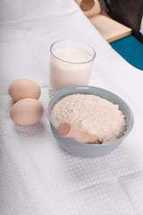 A glass of milk with raw eggs and a bowl of flour isolated on white background