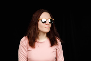 Image of sweet confident young lady standing over black background in studio, wearing pink blouse and fashionable eyeglasses, having long brown hair
