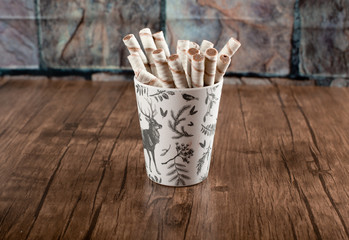 Waffle sticks in a cardboard cup on a wooden table.