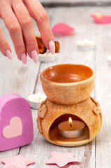 Obraz na płótnie Canvas Girl dripping essential oil into an aroma lamp.Aroma lamp with a burning candle and essential oils, pink salt bath bomb in the form of a heart, rose petals on a gray wooden table. Face and body care.