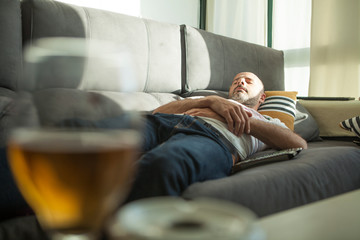 Hombre tomando la siesta en el sofa, despues de tomar cerveza - obrazy, fototapety, plakaty
