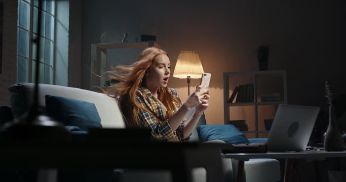 Astonished redhead caucasian girl looking at smartphone, wind blowing hair, Model reading breaking news, getting an amazing discount during online shopping or shocked by event 4k footage
