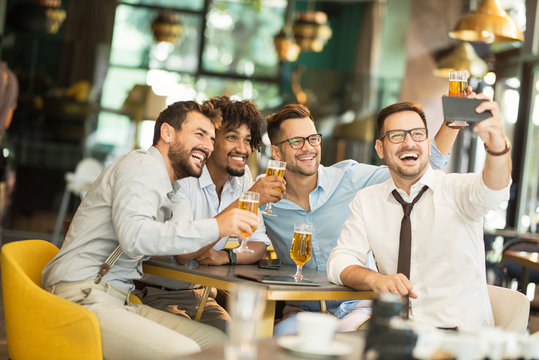 four businessmen having fun at the pub. Smiling businessmen sitting in cafe and taking photo on mobile. Best time is after working with colleagues