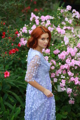 beautiful red-haired girl in arranger where azalea blooms in a colorful flying dress