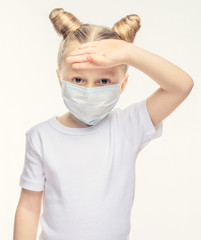 A little girl with blond hair in a medical mask touches her forehead with her hand. Medical concept of epidemiological period, respiratory diseases and high temperature.