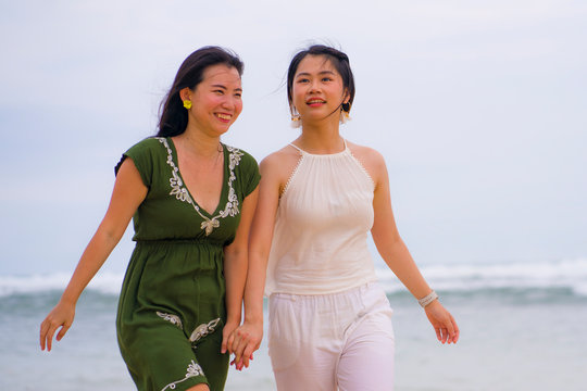 young beautiful and happy couple of attractive Asian Chinese women walking together relaxed at the beach enjoying holidays in gay lesbian love or close girlfriends relationship
