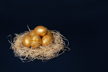 Golden colored Easter eggs in decorative nest on dark blue background. Happy Easter greeting card. Easter background. Place for text.