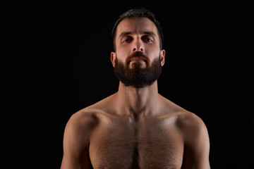Caucasian young man with beard, smiling subtly, shirtless, muscular body, on black background looking straight ahead, horizontal