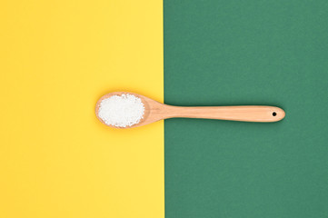 Wooden spoon with sea salt. On a yellow-green background. View from above. Place for writing