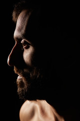 Caucasian young man with beard, no shirt, muscular body, looking away, silhouette, artistic pose, profile portrait, on black background, vertical