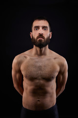 Fototapeta premium Caucasian handsome young man with a beard, serious, no shirt, muscular body,on black background looking straight ahead, vertical
