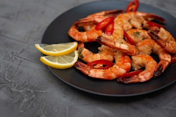 Tasty cooked fried shrimp with chilli and lemon on a gray concrete background. Healthy seafood. Flat lay.