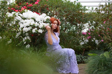 beautiful red-haired girl in arranger where azalea blooms in a colorful flying dress