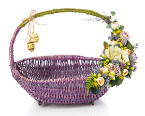Fototapeta na wymiar Original wicker basket of purple for Easter. Floral decor in olive tones with beige flowers, greens and hanging decorative eggs.