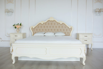 Bedroom in soft light colors. Big comfortable double bed in elegant classic bedroom
