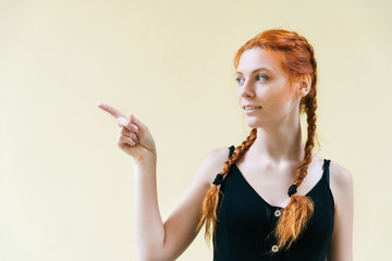 Obraz premium Expressive facial expressions emotions. Red haired girl in black dress on yellow background show finger to side.