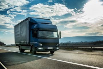 Fototapeta na wymiar Blue semi trailer truck on a highway driving at bright sunny sunset. Transportation vehicle