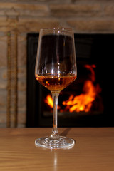 one glass of wine stands on a table in front of a fireplace, in which firewood burns with a bright flame, a concept of a romantic evening