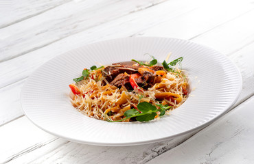 Pasta with beef, baked pepper and mushrooms on white wood background