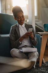 Happy African American entrepreneur typing text message on mobile phone.