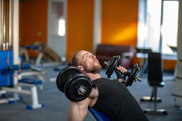 Naklejka na ściany i meble Strong man lifting weight in sport club. Closeup guy training muscles with dumbbells in gym. Handsome fitness trainer doing power lifting exercises in fitness center.