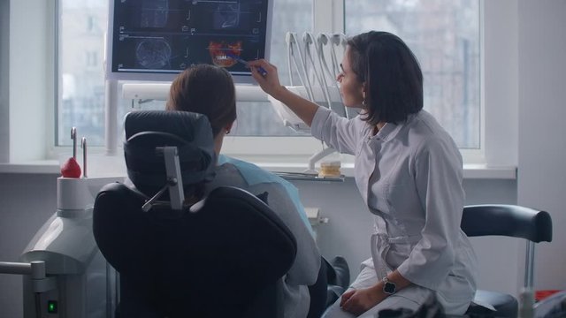 A female doctor discusses with the patient a plan for recovery and rehabilitation of the face after the accident looking at an x ray image on the monitor screen