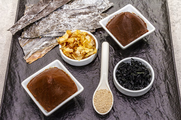 Set of traditional Japanese ingredient for cooking basic dashi broth. Algae kombu and wakame, miso paste, katsuobushi and dry granules. Black ceramic plate background