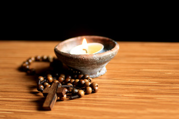 Rosary and candle on a table. Wooden rosary catholic with holy cross of Jesus Christ and candle...