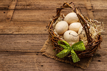 Easter wicker basket. Zero waste, DIY concept. Wooden eggs, shavings, satin bow. Old boards background