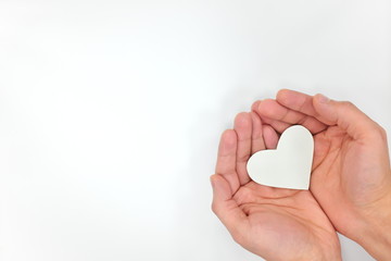 Hands holding a white heart in white background. Purity and kindness concept. Top view