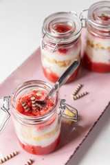 rot weißer Erdbeer Käse Sahne Kuchen im Glas mit Boden Biscuit auf rosa ovalem Teller
