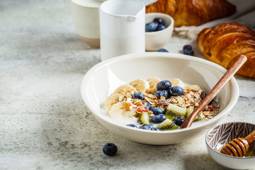 Breakfast muesli with fruits and croissants, gray background.