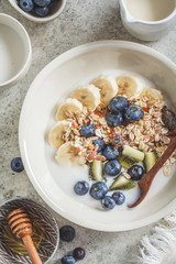 Muesli with yogurt, fruits and honey in white bowl, gray background.