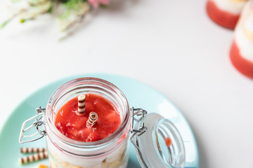 rot weißer Erdbeer Käse Sahne Kuchen im Glas mit Boden Biscuit auf hellblauen Teller