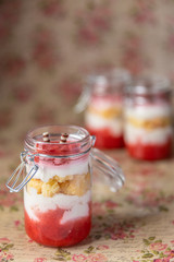 rot weißer Erdbeer Käse Sahne Kuchen im Glas mit Boden Biscuit auf geblümten Grund