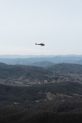 Fototapeta na wymiar Mount Comboyne - December 30th 2019: A helicopter drops water on a spot fire as seen from the top of Mount Comboyne.