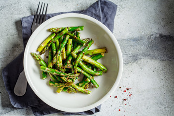 Cooked green asparagus with pepper and salt in a white bowl, top view.
