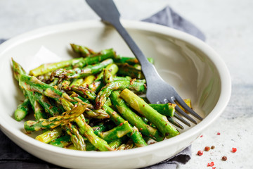 Cooked green asparagus with pepper and salt in a white bowl.