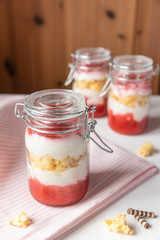 rot weißer Erdbeer Käse Sahne Kuchen im Glas mit Boden Biscuit auf hellem Grund mit rosa Küchentuch