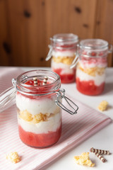 rot weißer Erdbeer Käse Sahne Kuchen im Glas mit Boden Biscuit auf hellem Grund mit rosa Küchentuch