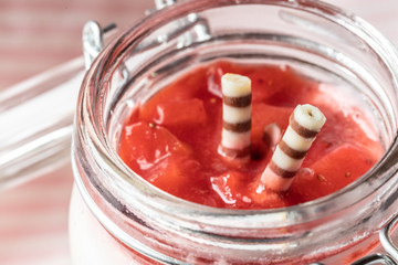 rot weißer Erdbeer Käse Sahne Kuchen im Glas mit Boden Biscuit auf hellem Grund mit rosa Küchentuch