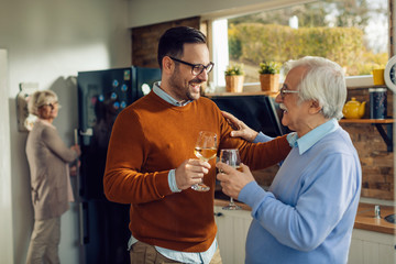 Cheerful mid adult man drinking wine with his senior father in the kitchen.