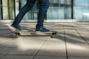 Fototapeta na wymiar Man skateboarding in city with one foot placed on board and pushing off with the other. Riding on longboard on paving stone. Selective focus on skateboard. Concept of leisure activity and urban.