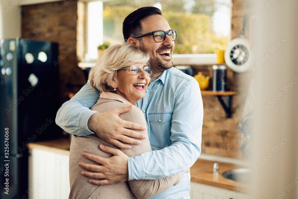 Wall mural Cheerful man and his mature mother embracing in the kitchen.