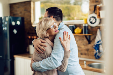 Happy senior woman embracing her adult son in the kitchen.