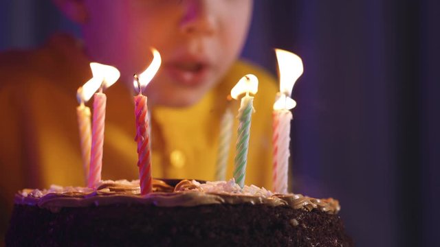 Cute boy blows out candles on a cake on his birthday.  Happy child looks at a cake with candles. Child looks at the cake and makes a birthday wish. Boy celebrates his birthday. Happiness concept