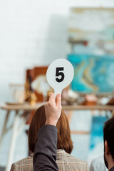 cropped view of buyer showing auction paddle with number five during auction
