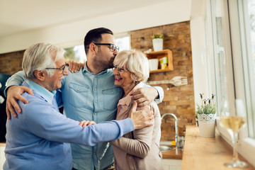 Affectionate man embracing his senior parents while greeting them in the kitchen.