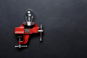 Light bulb clamped in mechanical hand vise on grey background with copy-space. Creative concept